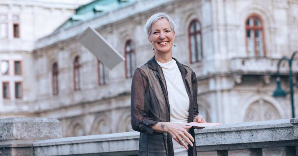 Expertin für Berufung finden Laya Commenda steht vor historischem Gebäude in Wien und wirft ein Journal in die Luft